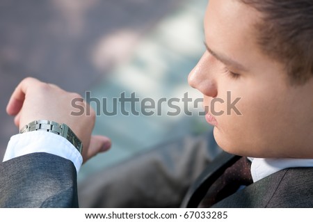 Young business man waiting for meeting at green park and looks at the watch. Student.