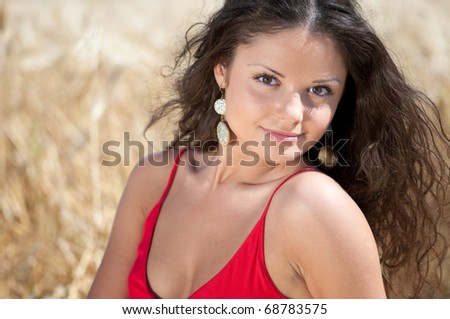Beautiful woman in red dress with perfect hair and skin posing in wheat field on sunny summer day. Picnic.