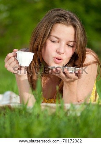 Beautiful young woman drink hot coffee outdoor on green grass