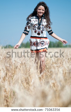 Beautiful woman in dress with perfect hair and skin walk in wheat field on sunny summer day.