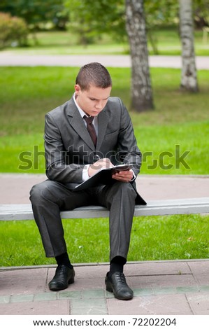Young business man waiting for meeting, working with papers at green park. Student.