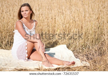 Beautiful woman in white dress with perfect hair and skin posing in wheat field on sunny summer day. Picnic.