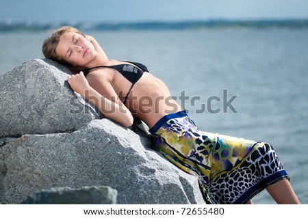 Beautiful sad woman in dress lying  on rock over storm sea and sky at summer day