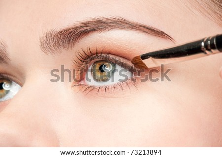 Beautiful young adult woman applying cosmetic paint brush - close-up portrait of eye shadow zone