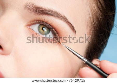 Beautiful young adult woman applying cosmetic paint brush - close-up portrait of eye shadow zone