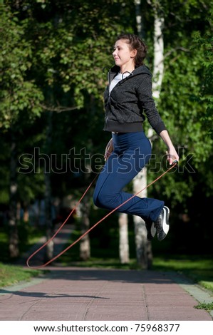 Beautiful young woman doing  exercise with skipping rope at park. Jumping