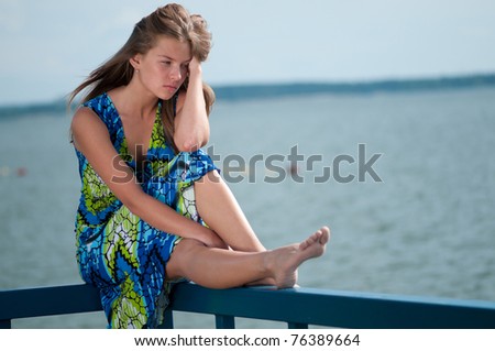 Beautiful sad woman in dress sitting  over sea at summer storm day