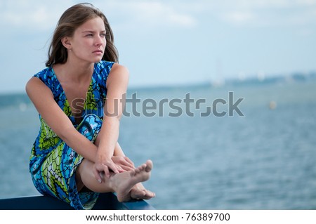 Beautiful sad woman in dress sitting  over sea at summer storm day