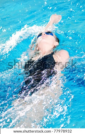 teenage girl swimming in swim meet doing backstroke