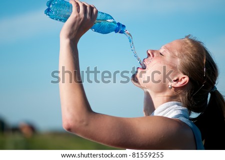 Beautiful young woman drinking water after exercise on sunny summer day