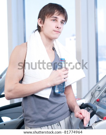 Young man at the gym exercising. Run on on a machine and drink water