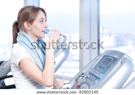 Young woman at the gym exercising. Run on on a machine and drink water