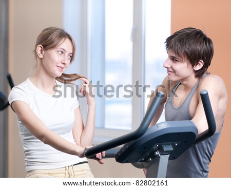 Woman and man train on machine in a gym assisted by personal instructor