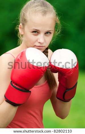 Beautiful young woman doing box exercise in red gloves at green park. Boxer