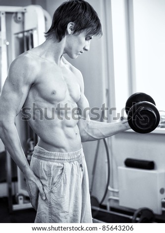 Fitness - powerful muscular man lifting weights in gym club