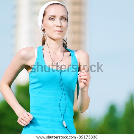 Beautiful woman with headphones running in green park on sunny summer day