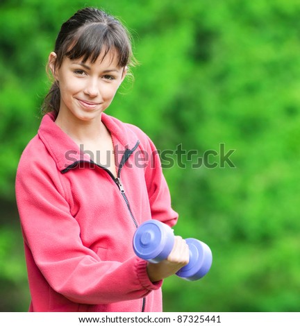 Beautiful teenage girl doing dumbbell exercise on green grass at park