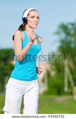 Beautiful woman with headphones running in green park on sunny summer day
