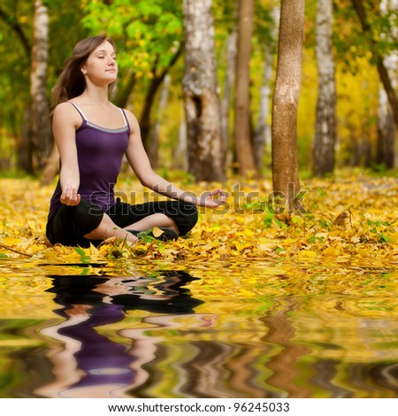 Young woman doing yoga exercises in the autumn city park lake. Fall with mirror in water