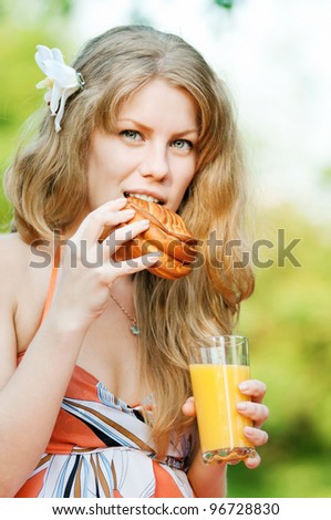 Young happy smiling woman drinking orange juice and eat roll outdoor