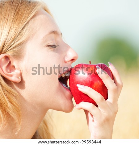 Young happy woman in wheat field with red apple. Summer picnic