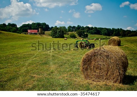 Bales of Hay and Farm Machinery with Red Farmhouse and Silo in Background