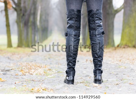 detail of woman wearing black clothes and boots in autumnal alley