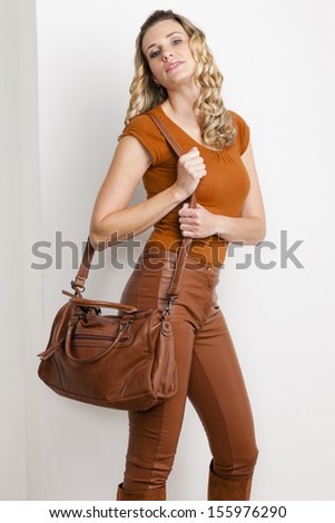 portrait of standing woman wearing fashionable brown clothes and boots with a handbag