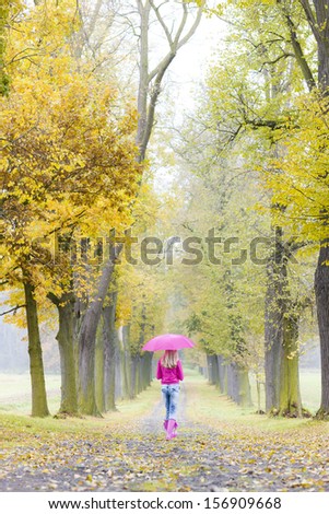 woman wearing rubber boots with umbrella in autumnal alley