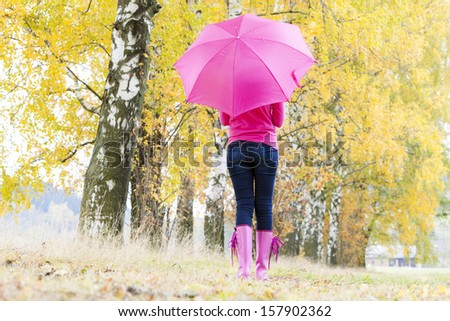 woman wearing rubber boots with umbrella in autumnal nature