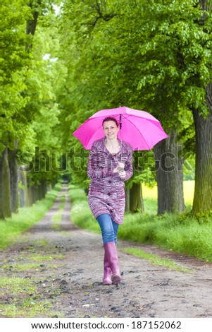 woman wearing rubber boots with umbrella in spring alley