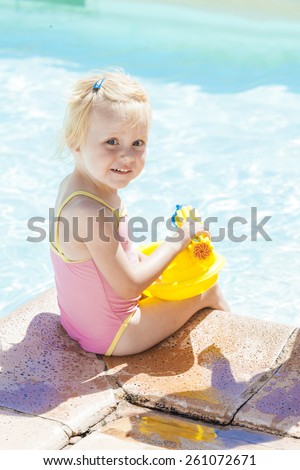little girl with water sprayer by swimming pool