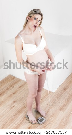 pregnant woman wearing lingerie standing on a weight scale with a tape measure
