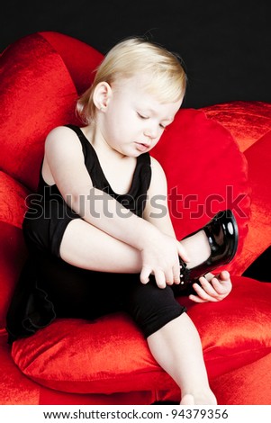 little girl with black shoes sitting on red armchair