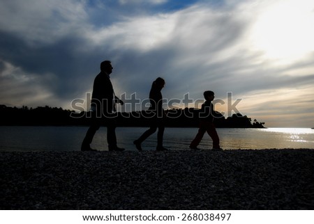 Silhouette of family walking on beach by the sunset. Horizontally framed shot.
