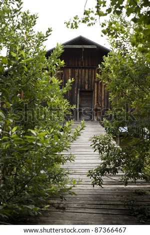 boat house situated right by the lakeshore and a pier leading to it seen through dense hedges