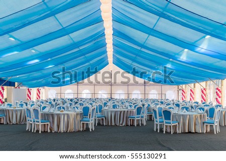 An empty banquet hall. Big tent with blue curtains, tables and chairs for a large number of guests. holiday decoration, dinner party.