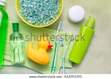 Bathroom accessories on a green towel. Rubber ducky, toothbrushes, soap and lotion. Baby care accessories for bath. Yellow duckling toy for kids.