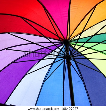 spokes and wires view of a rainbow and multicolour umbrella