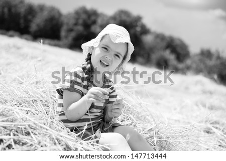 Little girl sitting in mown wheat. Black and white.