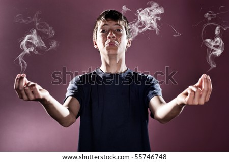 Young boy with smoke coming out of his mouth and hands. Actually he's smokin'. Studio shot, lens blur effect applied for selective focus.