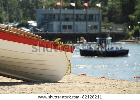 BOAT ON THE BEACH. A small row boat sits idle on the beach while a small passenger ferry boat passes by in the back ground.