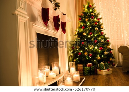Winter holidays atmosphere in a warm room with a christmas tree full of lights and toys near a cute fireplace with candles and present toys. Christmas interior. New year design.