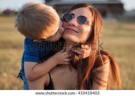 The son kisses and hugs his mom in sunglasses outdoors. Mother and her child having fun together. Little kid express the love to his young mommy.