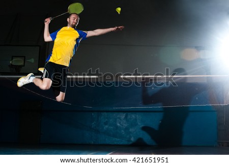 Bearded  badminton player in sport outfit jumping and making a racket swing on the fly. Artistic studio lighting and lens flare effect.