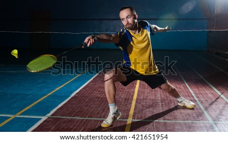 Bearded  badminton player in sport outfit reaching for a shuttle with a racket swing. Artistic studio lighting and lens flare effect.