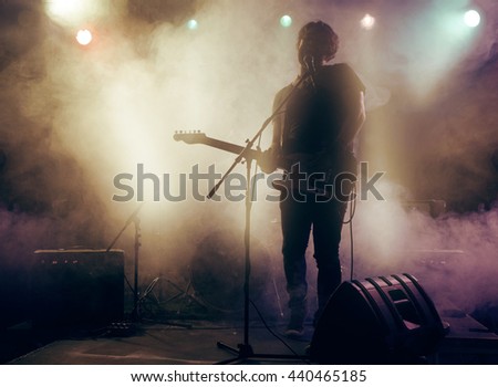 Silhouette of guitar player on stage. Dark background, smoke, spotlights