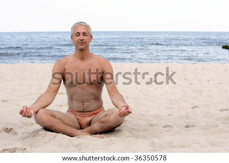Portrait of handsome mature man meditating in lotus position on the beach