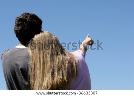 Romantic teenage couple looking at blue sky. Girl pointing.