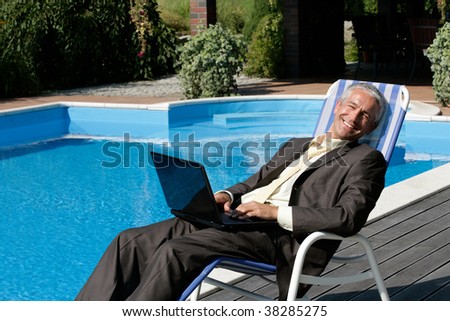 Businessman with laptop computer resting on deck chair next to swimming pool